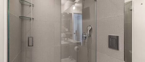 Une douche moderne dotée d’un pare-douche en verre, d’un pommeau de douche à main et d’un panneau de commande fixé au mur.