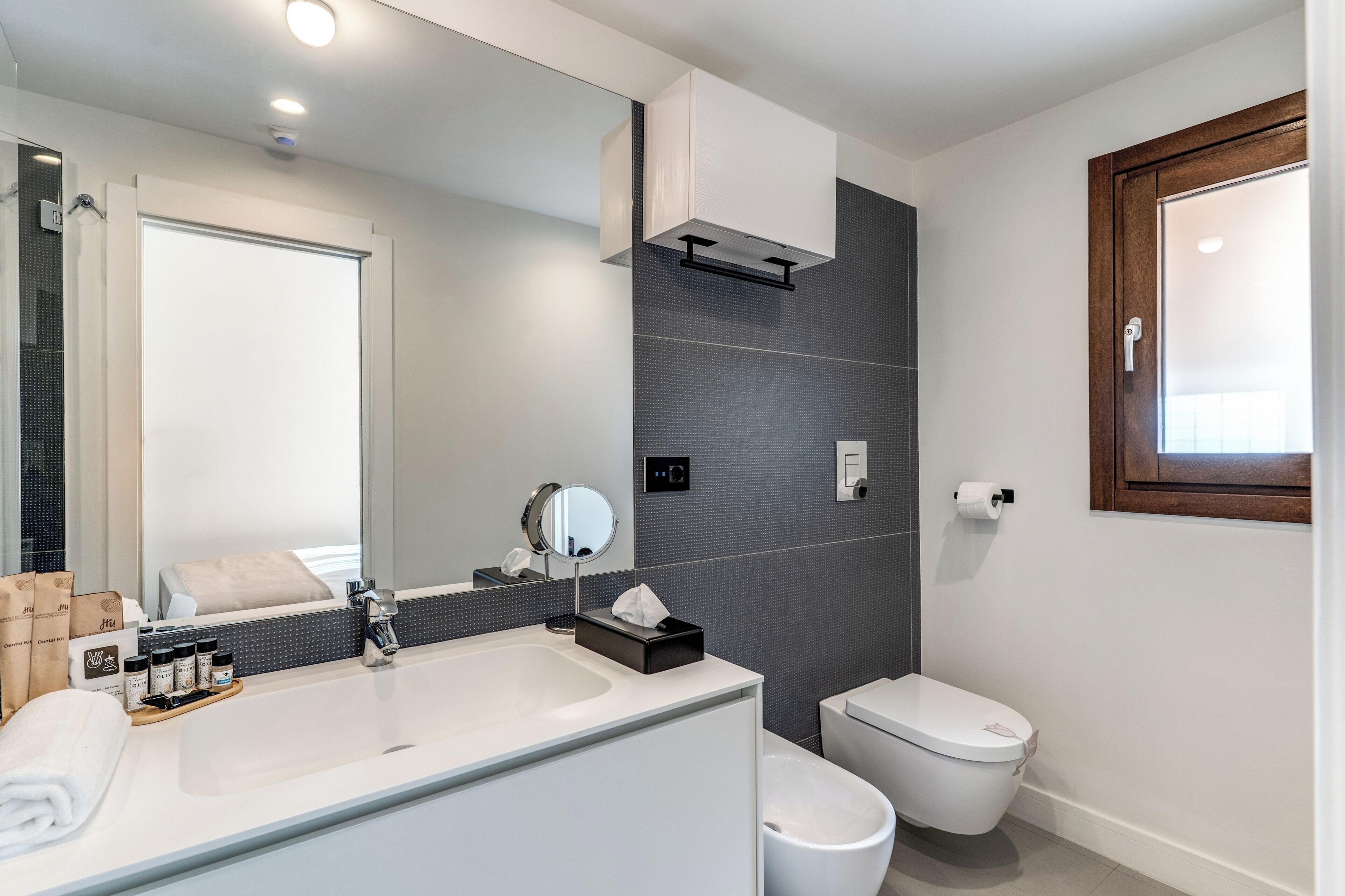 Une salle de bain moderne avec un grand miroir, un lavabo, des toilettes et une fenêtre.