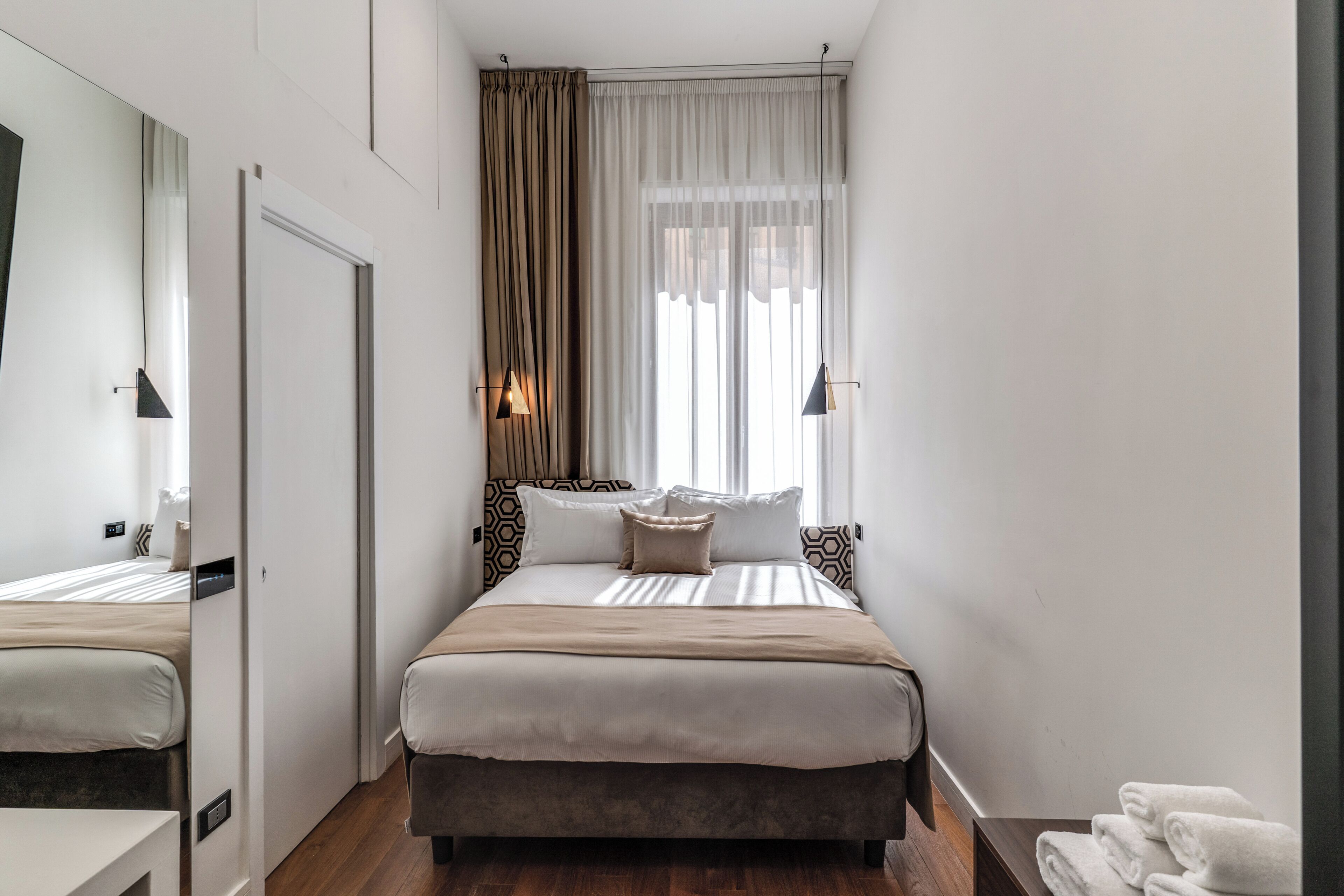 A bedroom with a bed, bedside tables, a mirror, a window with curtains, and a towel rack.