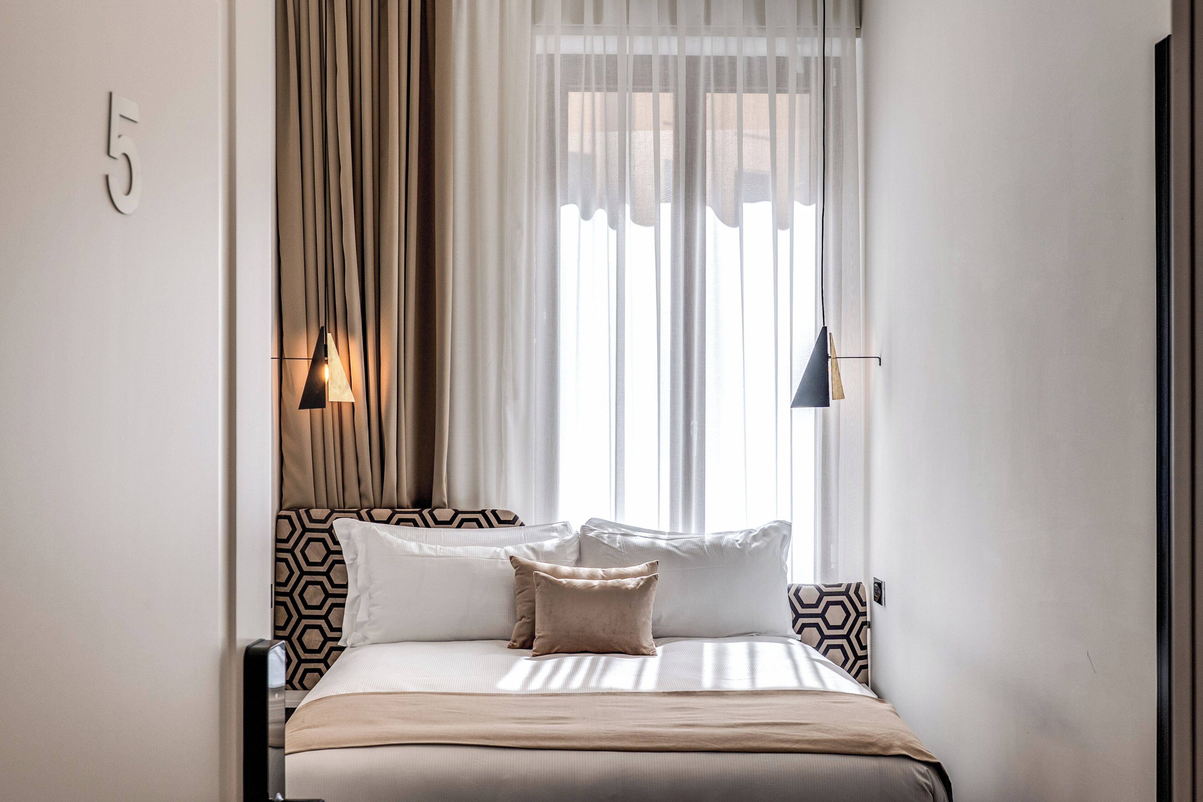 A bedroom with a bed, curtains, and a wall-mounted light fixture.