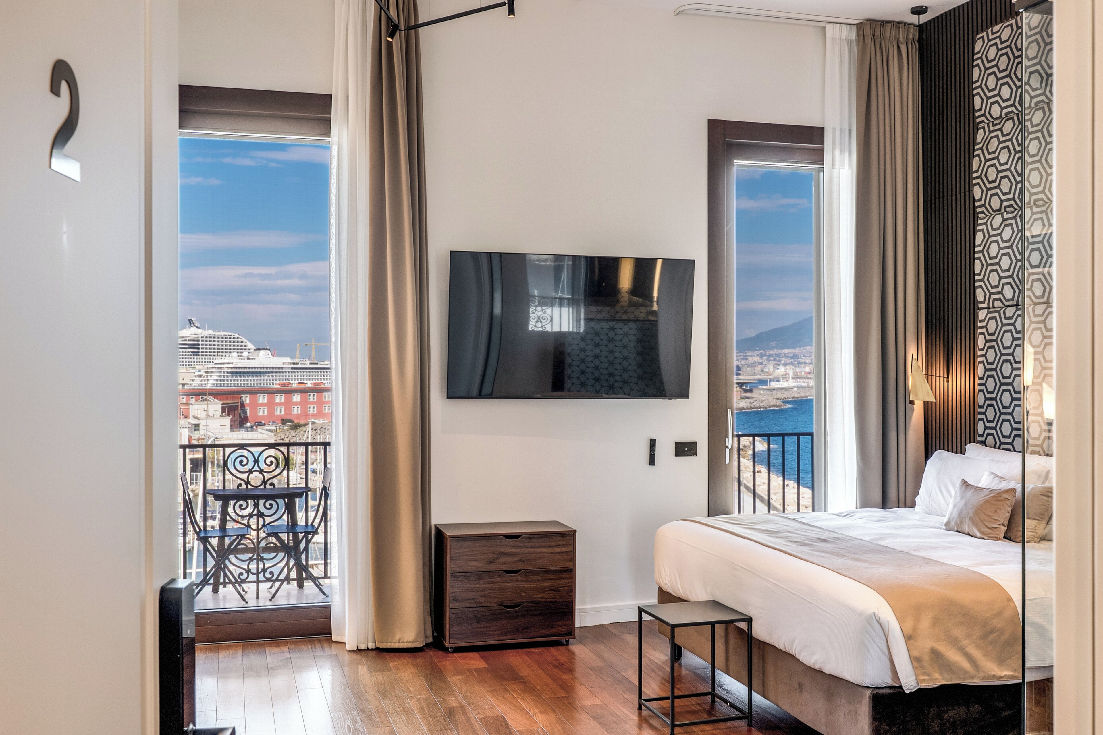 Une chambre à coucher comprenant un lit, une télévision, une table de chevet, une chaise et un balcon avec vue sur la ville.