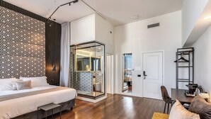 Een moderne hotelkamer met een groot bed, een zithoek met een bank, een klein tafeltje en een inloopkast met een spiegel.