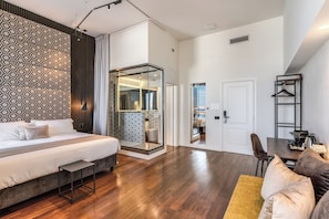 Moderni hotellihuone, jossa on suuri sänky, oleskelualue sohvineen ja pieni pöytä sekä erillinen vaatehuone peilillä.