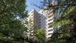 Um edifício com várias andares e varandas, rodeado por árvores e vegetação.