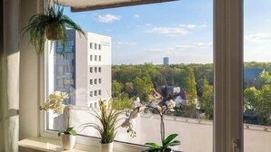 Uma janela com vista para um edifício identificado como "S.V. Goronk" e uma varanda com vasos de plantas.