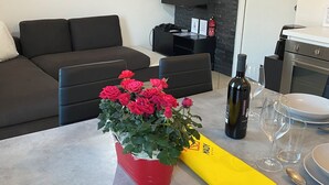 Un soggiorno moderno con divano, un quadro astratto rosso, televisore a schermo piatto, camino e zona pranzo con una bottiglia di vino e bicchieri.