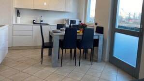 Una cucina moderna con mobili bianchi, un tavolo da pranzo con sedie, un forno a microonde e una finestra con vista sugli edifici.