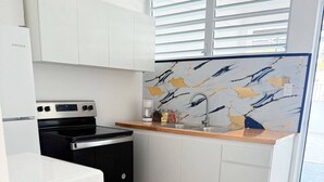 A kitchen with white cabinets, a black stove, a white refrigerator, a wooden countertop, and a tiled floor. - Charming 3BR Near Ponce Attractions (Ponce)
