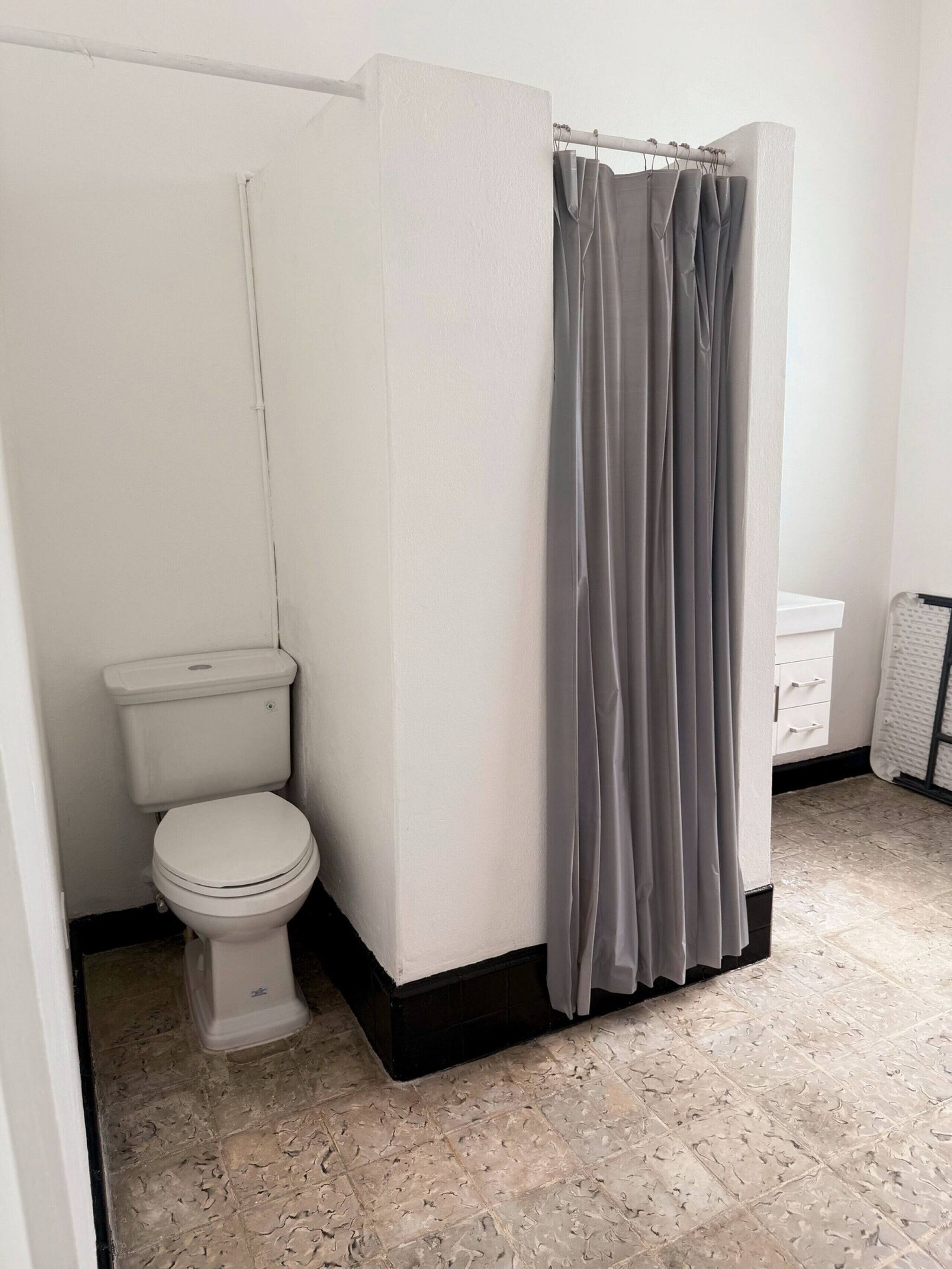 Un baño con inodoro, cortina de ducha y suelo de baldosas.