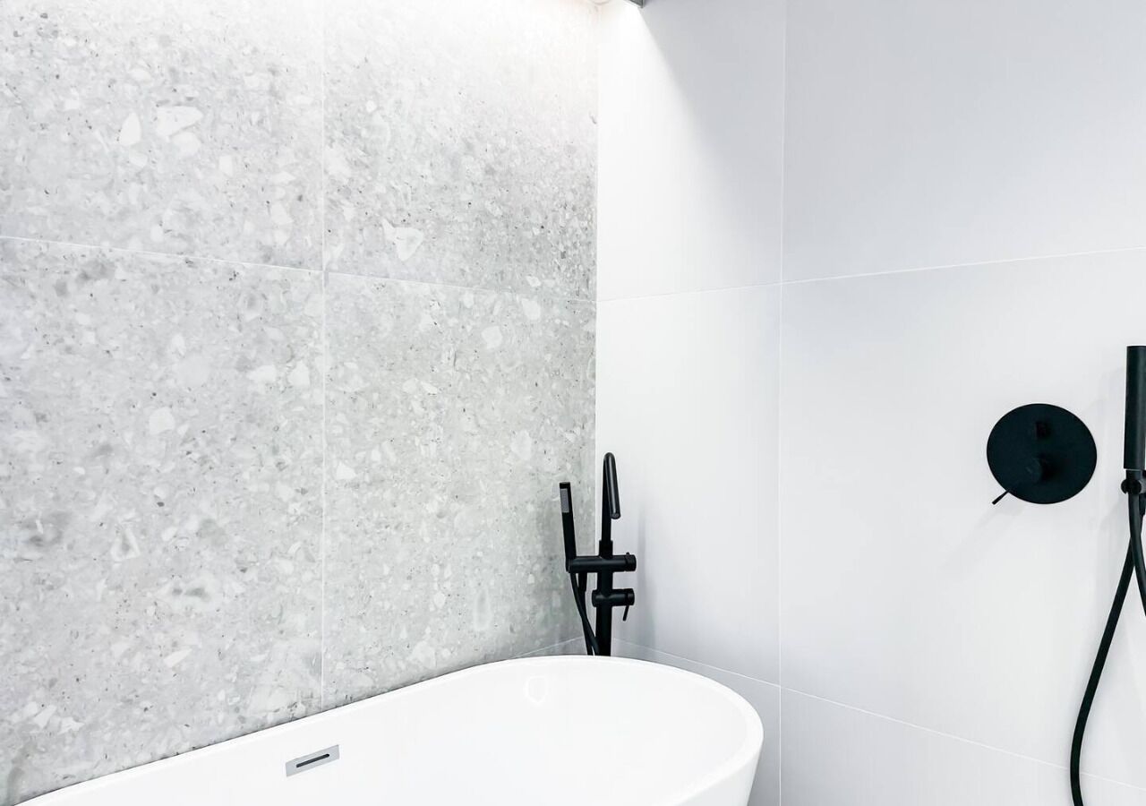 A bathroom with a white sink, a marble wall, and a black faucet.
