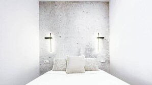 Une chambre moderne avec un mur d’accent en béton, un lit avec une literie blanche et deux appliques murales.