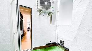 Un couloir étroit doté d’un sol recouvert d’un gazon artificiel vert, de murs blancs et d’une porte blanche donnant sur une pièce.
