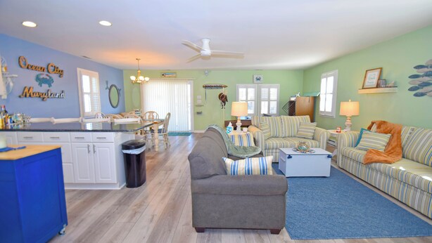 A living room with a gray sofa, striped couches, a coffee table, and a dining area with a table and chairs. - Montego Bay-Colonial Drive 13339-Bayside 135th Street (pets allowed) (Ocean City)