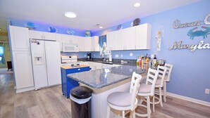 A kitchen with white cabinets, a granite island, and a blue accent wall with 'Ocean Maryland' decor. - Montego Bay-Colonial Drive 13339-Bayside 135th Street (pets allowed) (Ocean City)