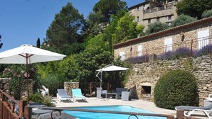 Un espace piscine agrémenté de chaises longues et de parasols, entouré de murs en pierre et de verdure.