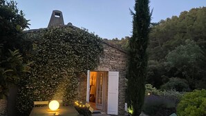 Une charmante maison en pierre dotée d’une terrasse en bois, d’une table avec des chaises et d’un éclairage chaleureux.