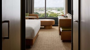 Een hotelkamer met een groot raam, een bed, een bureau, een stoel en een televisietoestel.