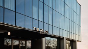 Een modern hotelgebouw met een reflecterende glazen gevel en de naam "The Atlas Hotel" duidelijk zichtbaar bij de ingang.
