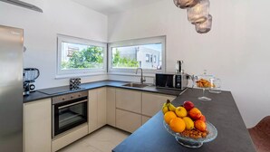 Eine moderne Küche mit Backofen, Mikrowelle und Kaffeemaschine. Zwei Fenster sorgen für natürliches Licht, und auf der Arbeitsfläche steht eine Obstschale.