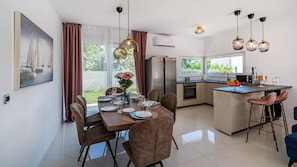 A modern kitchen with a central island, a dining area with a table set for four, and a large window offering a view of the outdoors.
