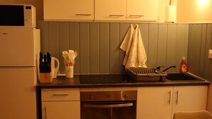 Una cucina compatta con mobili bianchi, lavastoviglie integrata e forno a microonde. Si nota un lavello con rubinetto, un portascopini e una bottiglia di detersivo per piatti sul piano di lavoro.