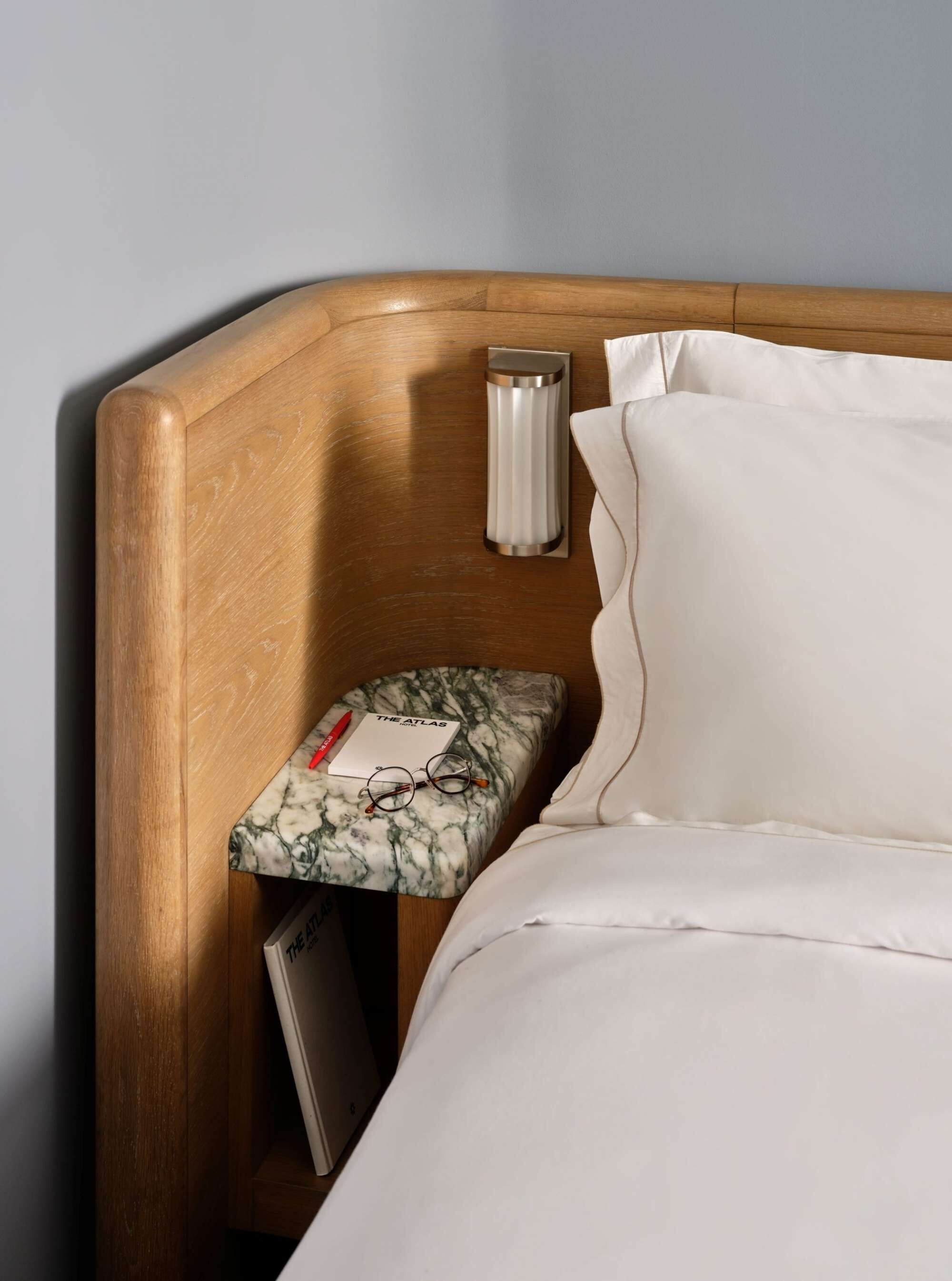 A neatly made bed with white linens, a wooden headboard, and a bedside table with a marble-patterned cushion.