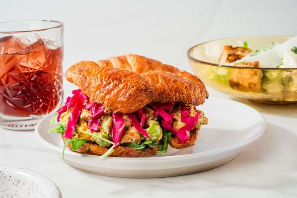 Un sandwich au pain croustillant, garni de légumes verts et de chou rouge, servi sur une assiette blanche.