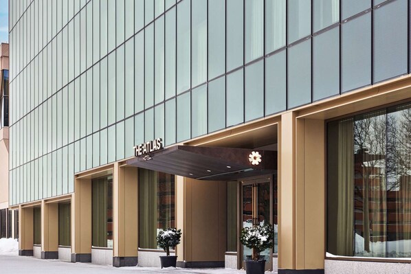 A modern hotel facade with a large entrance, large windows, and a sign reading "The Atlas Hotel". - By Charles River | Luxe Stay. Fitness + Dining (Boston)