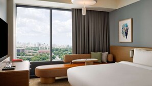 Habitación de hotel con una cama grande, zona de estar, vistas a la ciudad y un cuadro en la pared.