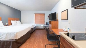 Une chambre d’hôtel avec deux lits, un bureau, une chaise, une télévision et une kitchenette.