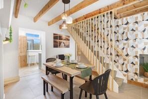 Zona pranzo con tavolo e sedie in legno, una scala con pareti a motivi geometrici e vista sull'esterno.