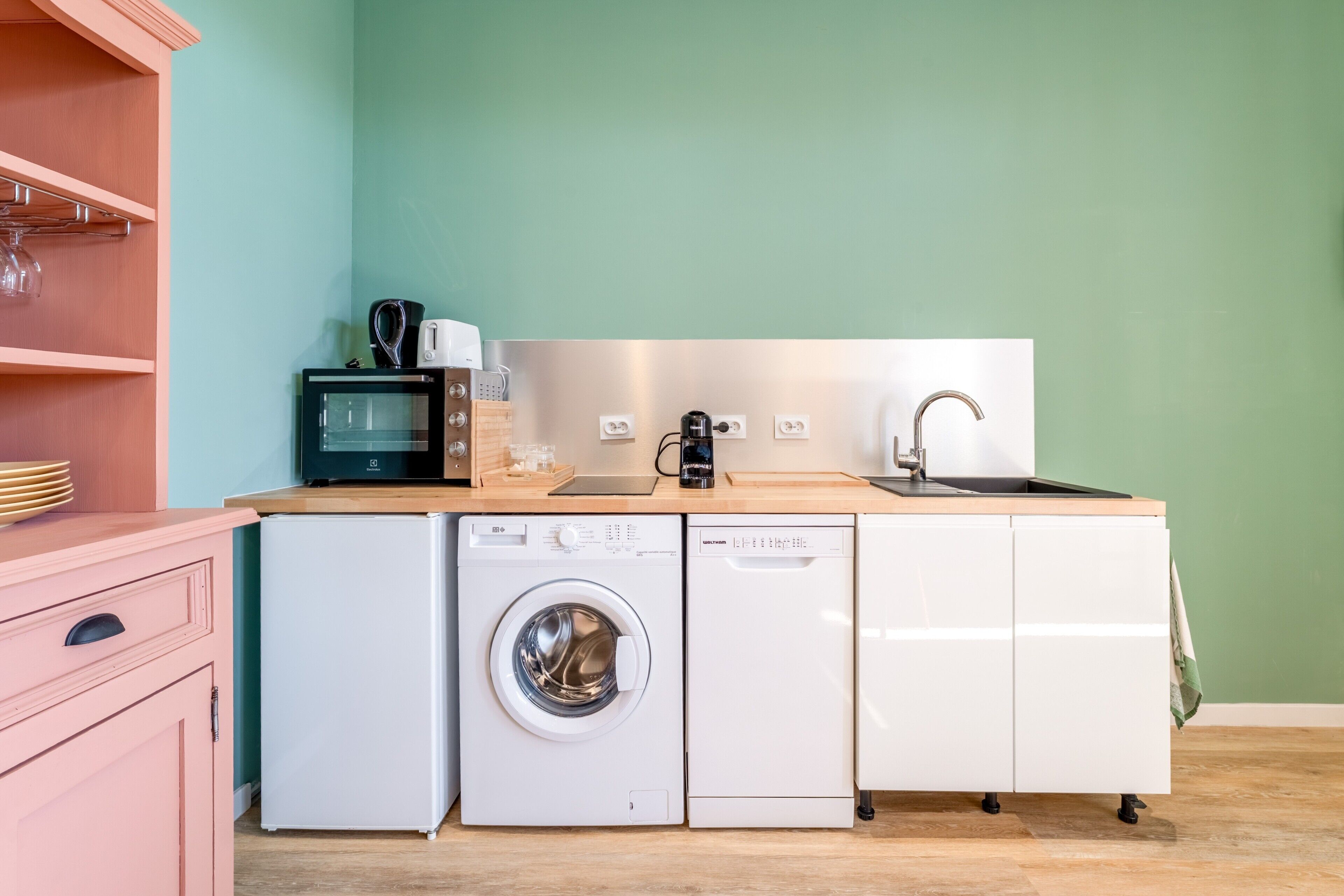 A compact kitchen with a washing machine, a coffee maker, and a sink.