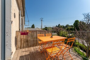 Terraza de madera con mesa y sillas, valla de madera, y vistas a árboles y una carretera.