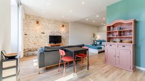 A modern living room with a stone wall, a flat-screen TV, a sofa, a dining table with chairs, and a pink cabinet. - Holiday Home 'La halte provençale - Cocooning' with Private Terrace, Wi-Fi & Air Conditioning (Châteaurenard)