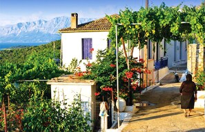 A rural village with a white building, a person walking down a path, and mountains in the background. - Elegant Waterfront Villa with Uninterrupted Ionian Views and Direct Sea Access (Meganissi)