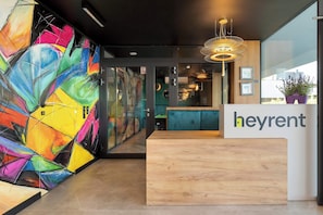 Un moderno mostrador de recepción con un mural abstracto lleno de color, una zona de recepción de madera y vistas a la ciudad a través de amplias ventanas.