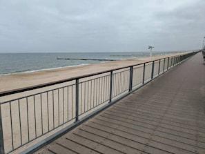 Una pasarela de madera con barandas de metal que lleva a una playa de arena y al océano.
