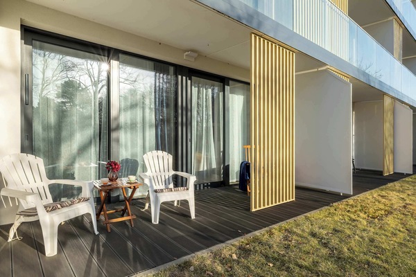 A spacious terrace with two white chairs and a small table for outdoor dining. A wooden privacy screen separates the space from neighboring units.