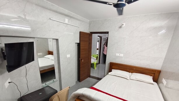 A bedroom with a bed, a desk, a chair, a mirror, and a ceiling fan. - VJ Homes (Puducherry)