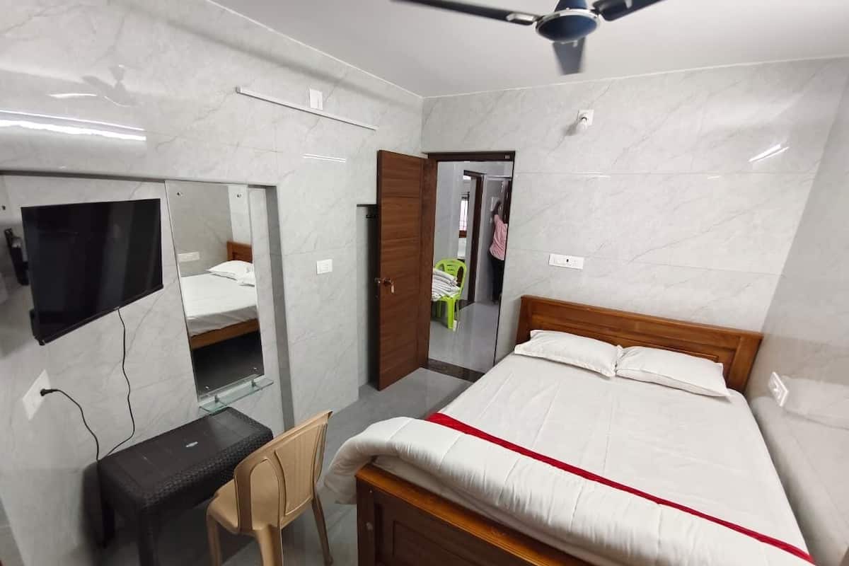 Ein Schlafzimmer mit einem Bett, einem Schreibtisch, einem Sessel, einem Spiegel und einem Deckenventilator.