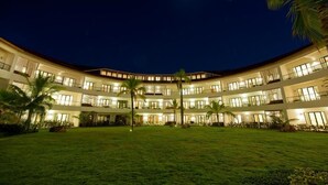 Un hotel de varios pisos con un patio central, palmeras y un cielo nocturno con luna visible.
