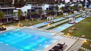 Un resort moderno con una amplia piscina, zonas de descanso y palmeras.