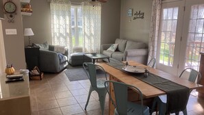 Ein Wohnzimmer mit einer Couch, einem Esstisch mit Stühlen, einem Deckenventilator und einem Fenster mit Vorhängen.