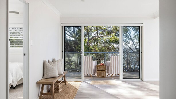 Une chambre moderne dotée d’une grande porte-fenêtre coulissante donnant sur un balcon, d’un banc en bois et d’une chaise à rayures.