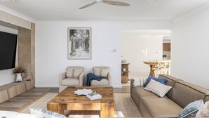 Un salon comprenant une table basse, deux fauteuils, un canapé, un téléviseur et un tableau encadré accroché au mur.