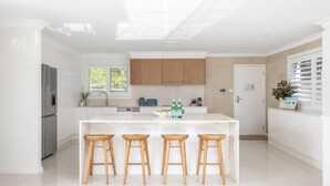 Une cuisine moderne dotée d’un îlot central, de tabourets en bois et offrant une vue sur l’extérieur.