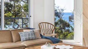 A room with a leather sofa, a wooden chair, a coffee table, and a view of the sea. - Dutchies Getaway – Elegant Family Home by the Water (Nelson Bay)