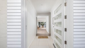 Un couloir aux murs blancs, doté d’un plancher en bois et d’une porte en verre sur le côté droit.