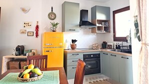 Eine kleine Küche mit einem gelben Kühlschrank, einem Holzespeisetisch mit Obstkorb und einem Fenster mit Vorhängen.
