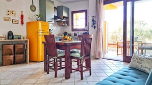 Ein gemütliches Wohnzimmer mit einem blauen Sofa, einem Esstisch mit Stühlen, einer Küchenzeile mit einem gelben Kühlschrank und einer Glasschiebetür, die auf eine Außenpatio führt.